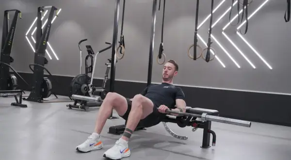 Man utför hip thrust med skivstång på en bänk i ett modernt gym.