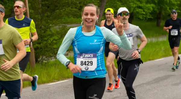 Glada löpare kämpar på en mil. En kvinna med nummer 8429 ler och gör segertecken.