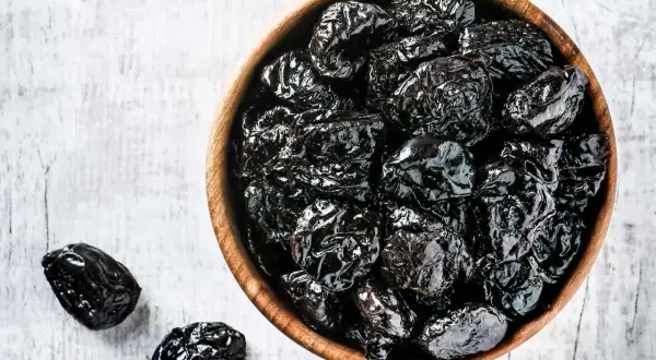 En skål med torkade plommon, som är nyttigt och gott. Några plommon ligger bredvid på en vit bakgrund.