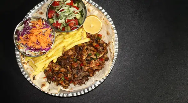 En stor portion kebabpizza med pommes frites, sallad och citron. En rejäl måltid, men tänk på kebabpizza kalorier!