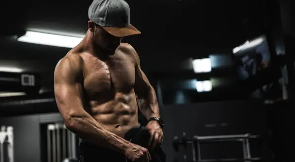 Muskulös man i gym, visar upp sina magrutor. Frågan "hur får man magrutor" besvaras med dedikation och träning.