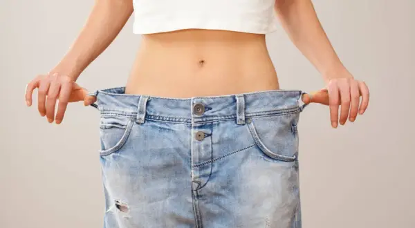 En person visar upp sina för stora jeans, ett tydligt tecken på att de lyckats gå ner i vikt.
