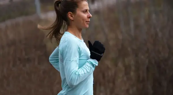 Kvinna i ljusblå tröja och svarta handskar springer utomhus, fokuserad på att sätta ett nytt maraton rekord.