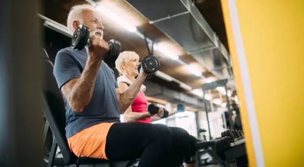 Äldre par tränar med hantlar på gym. De visar att sarkopeni betyder minskad muskelmassa, men att träning kan motverka detta.
