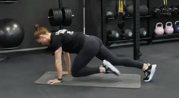 Kvinna gör mountain climbers på en träningsmatta i ett gym. Hon verkar ha dålig kondition, men kämpar på.
