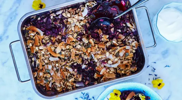 En härlig, nyttig dessert med bär och granola i en ugnsform. Serveras med en klick yoghurt och garnerad med blommor.