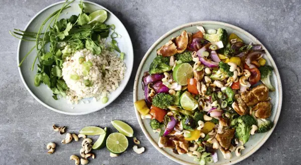 Två tallrikar med nyttig grillmat: ris med koriander och grönsaker, samt en wok med kyckling, broccoli, paprika, cashewnötter och lime.