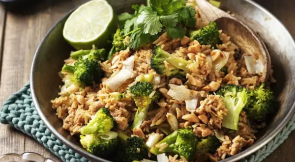 En skål med stekt ris med broccoli, jordnötter och en limeklyfta. En perfekt nyttig lunch.
