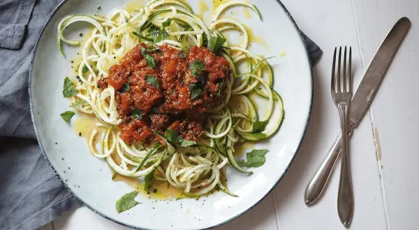En tallrik med zucchini-spaghetti och köttfärssås, ett av många zucchini nyttiga recept. Garnerad med färska örter och en gnutta citronzest.