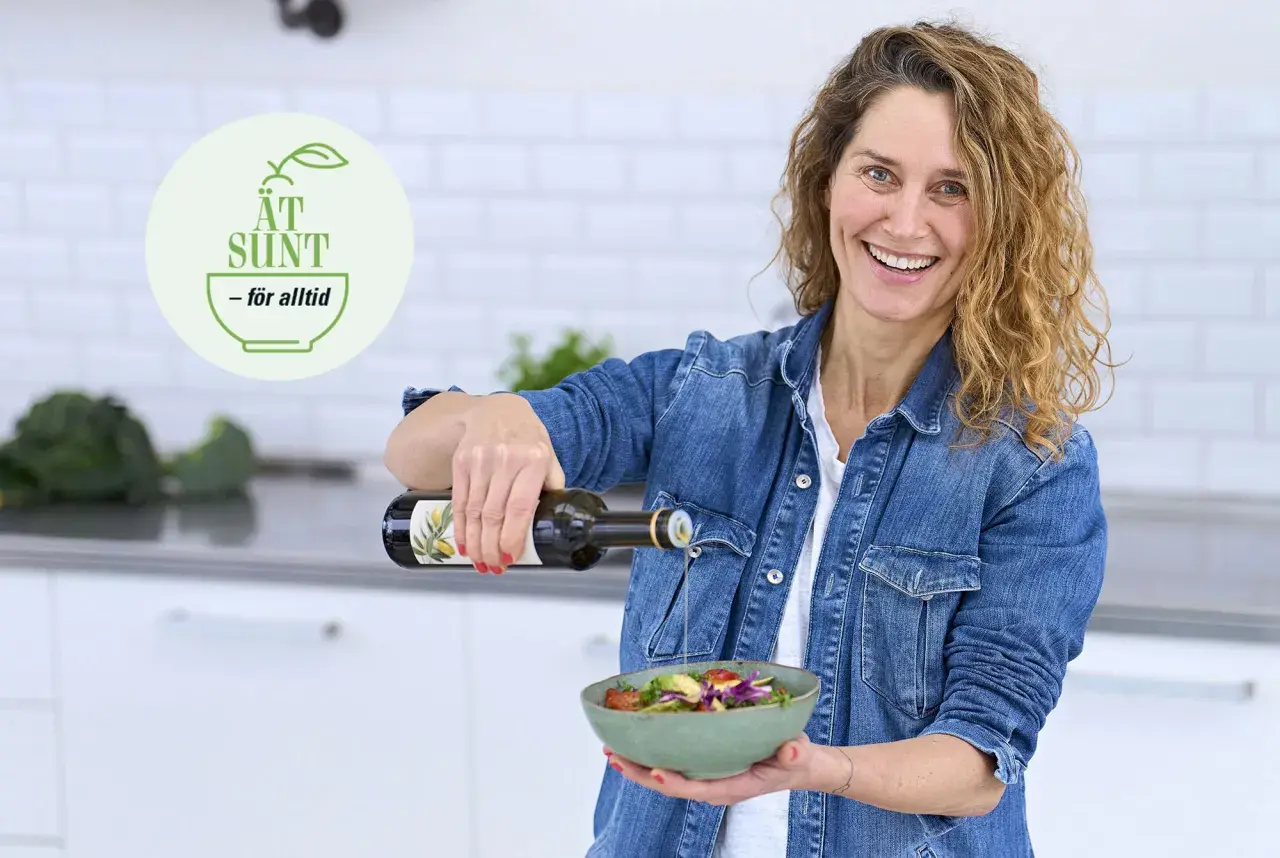 Glad kvinna häller olivolja över en fräsch sallad. En logotyp med texten "ÄT SUND - för alltid" syns i bakgrunden, vilket antyder en livsstil med fet mat och hälsosamma val.
