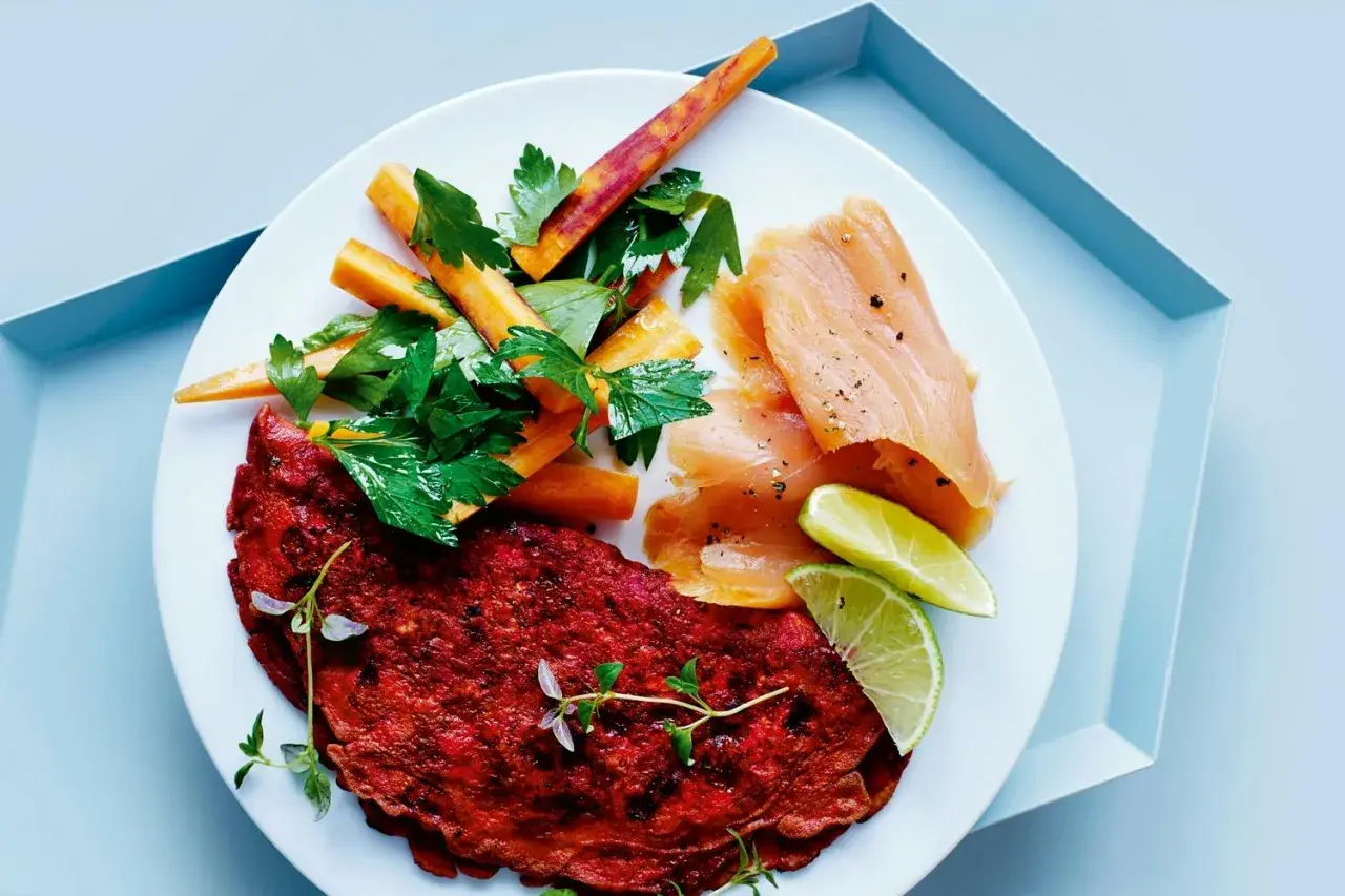 En tallrik med en röd omelett, rökt laxprotein, morotsstavar och limeklyftor.
