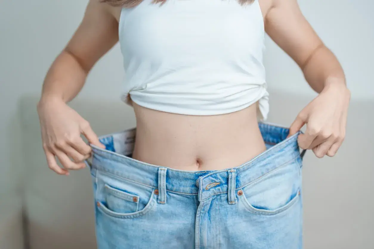En person visar upp sina för stora jeans, ett tecken på att hon lyckats med hur man går ner i vikt.