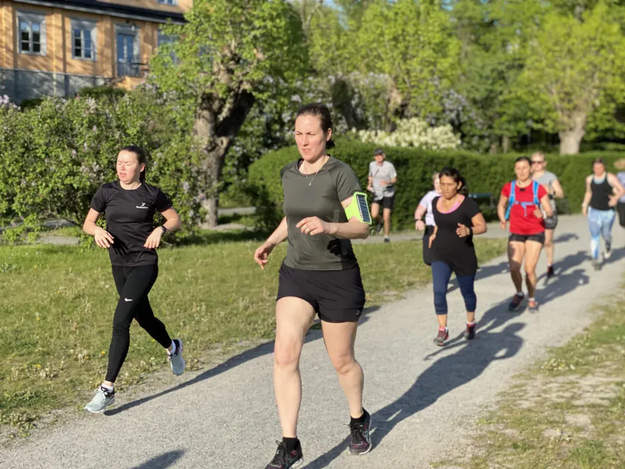 En grupp löpare, mestadels kvinnor, tar sig fram på en grusväg i en park. De är på väg att springa en mil i det vackra vårvädret.