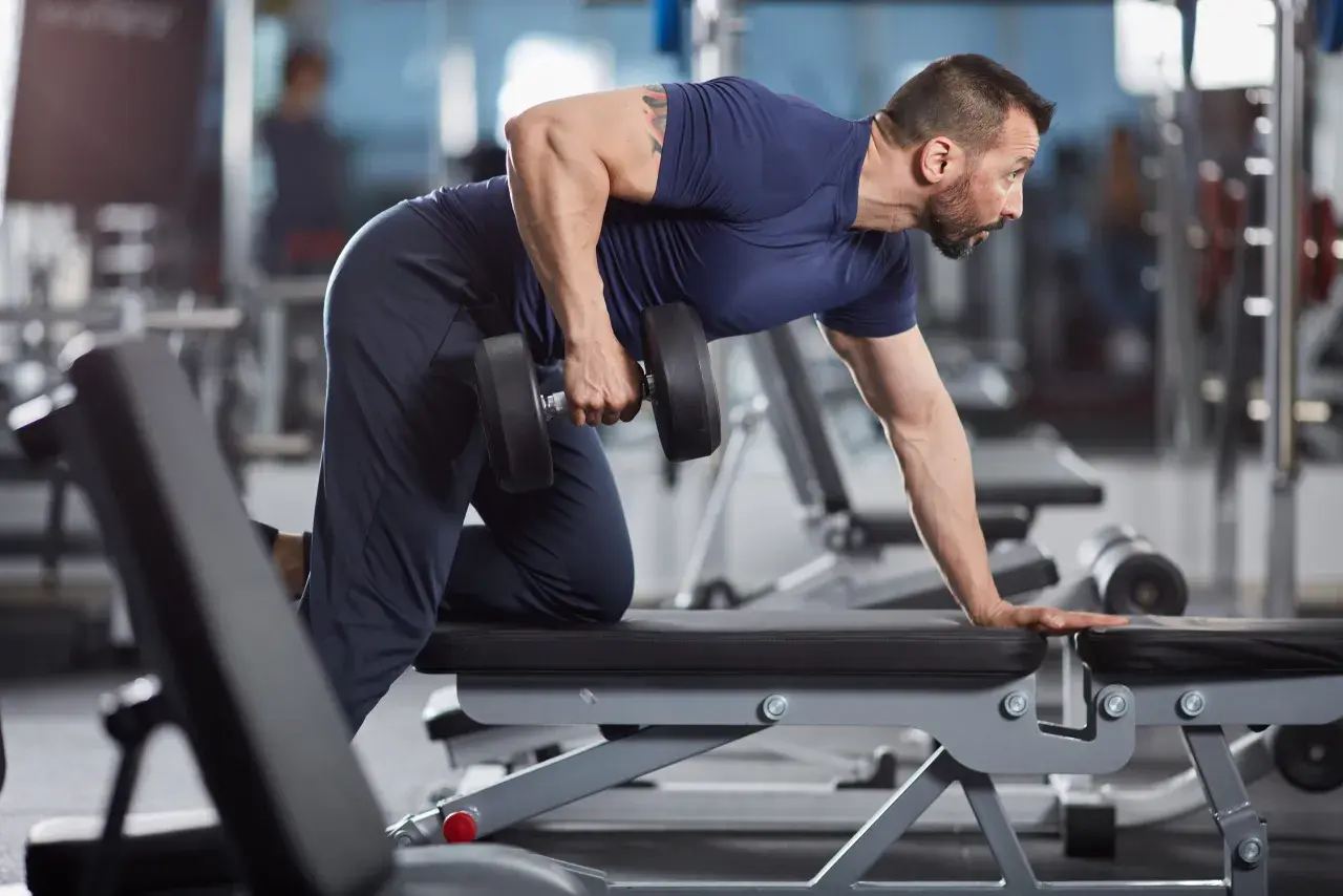 Man utför enarms hantelrodd på en träningsbänk i ett gym.