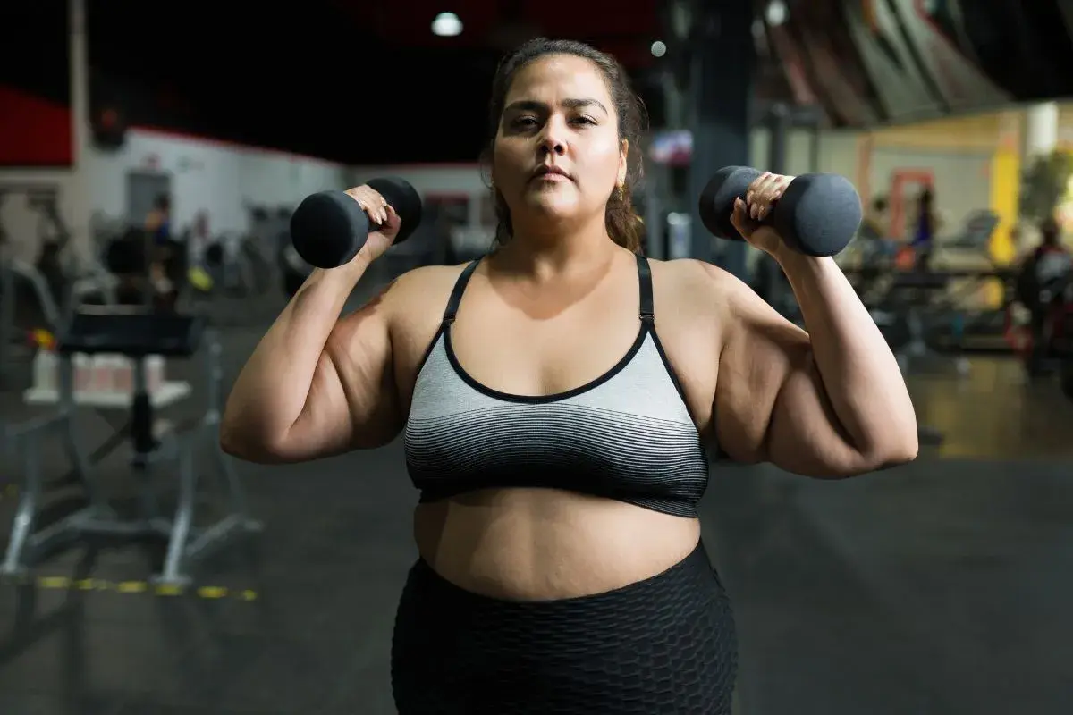 En kvinna lyfter hantlar på gymmet, en del av hennes träningsresa för att gå ner i vikt.