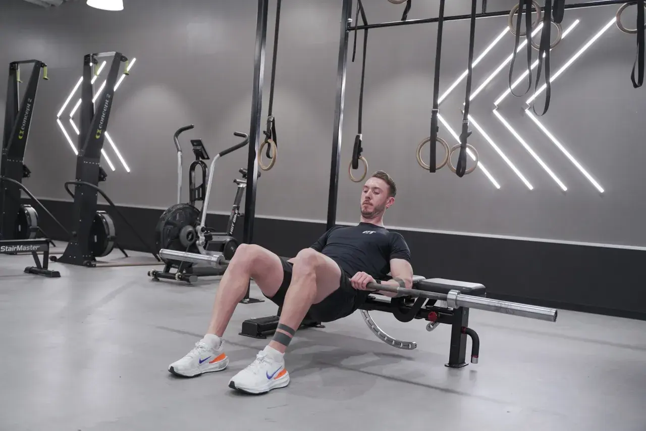 Man utför hip thrust med skivstång på en bänk i ett modernt gym.