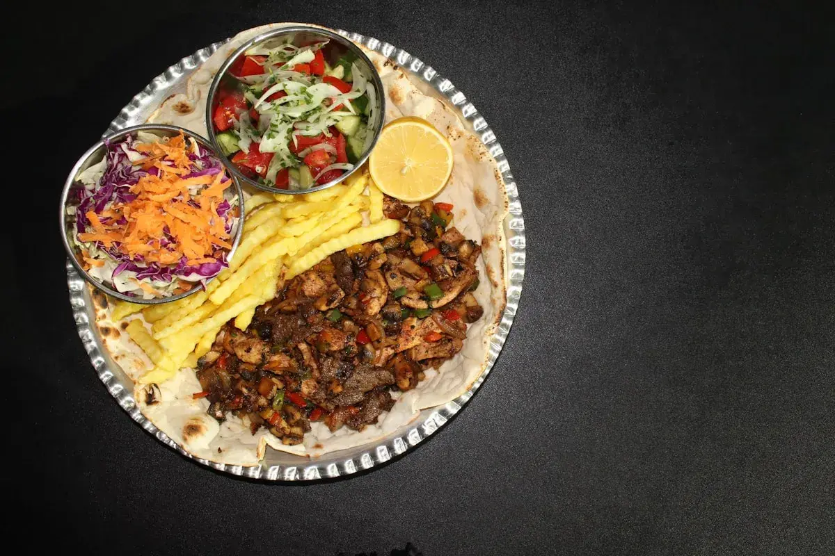 En stor portion kebabpizza med pommes frites, sallad och citron. En rejäl måltid, men tänk på kebabpizza kalorier!