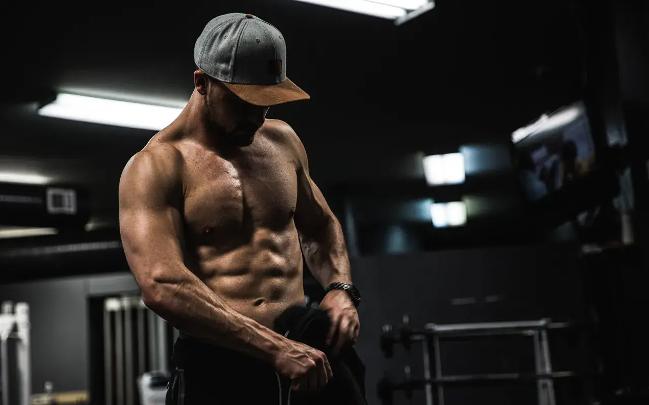 Muskulös man i gym, visar upp sina magrutor. Frågan "hur får man magrutor" besvaras med dedikation och träning.