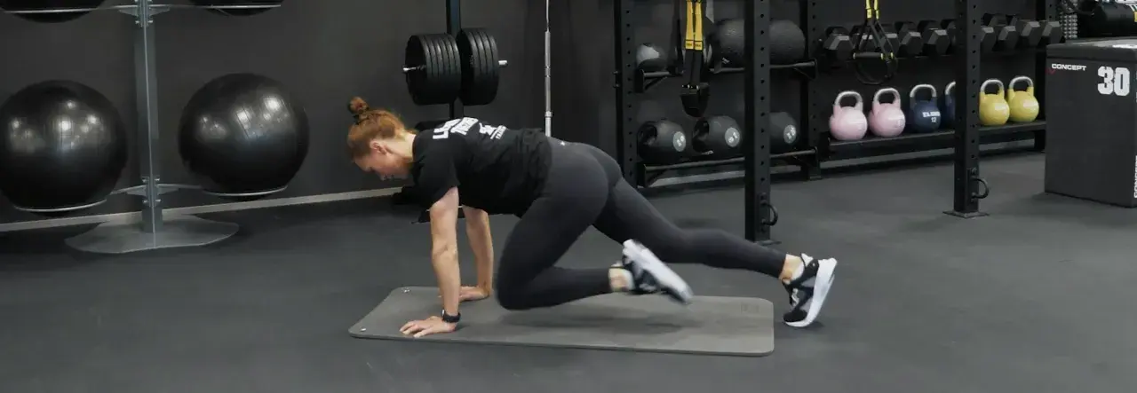 Kvinna gör mountain climbers på en träningsmatta i ett gym. Hon verkar ha dålig kondition, men kämpar på.