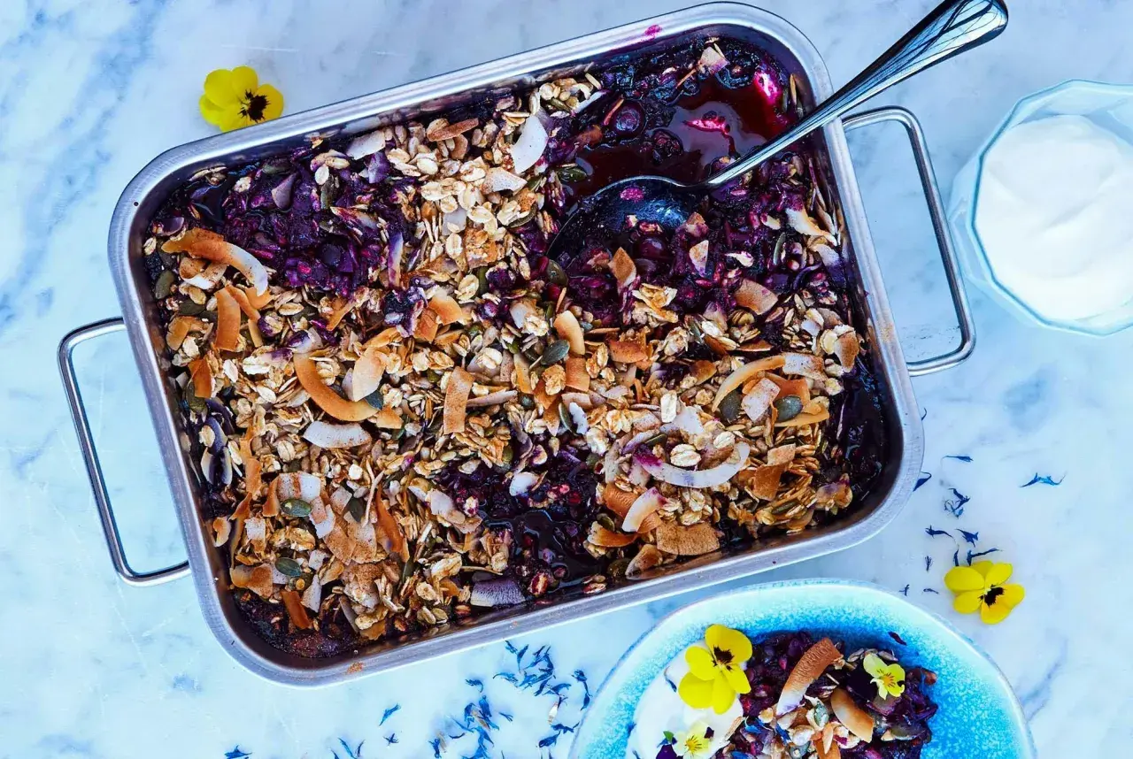 En härlig, nyttig dessert med bär och granola i en ugnsform. Serveras med en klick yoghurt och garnerad med blommor.