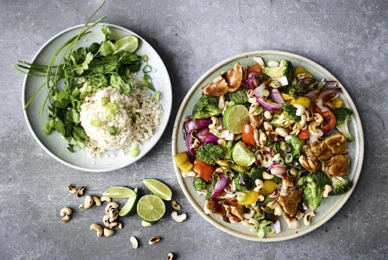 Två tallrikar med nyttig grillmat: ris med koriander och grönsaker, samt en wok med kyckling, broccoli, paprika, cashewnötter och lime.