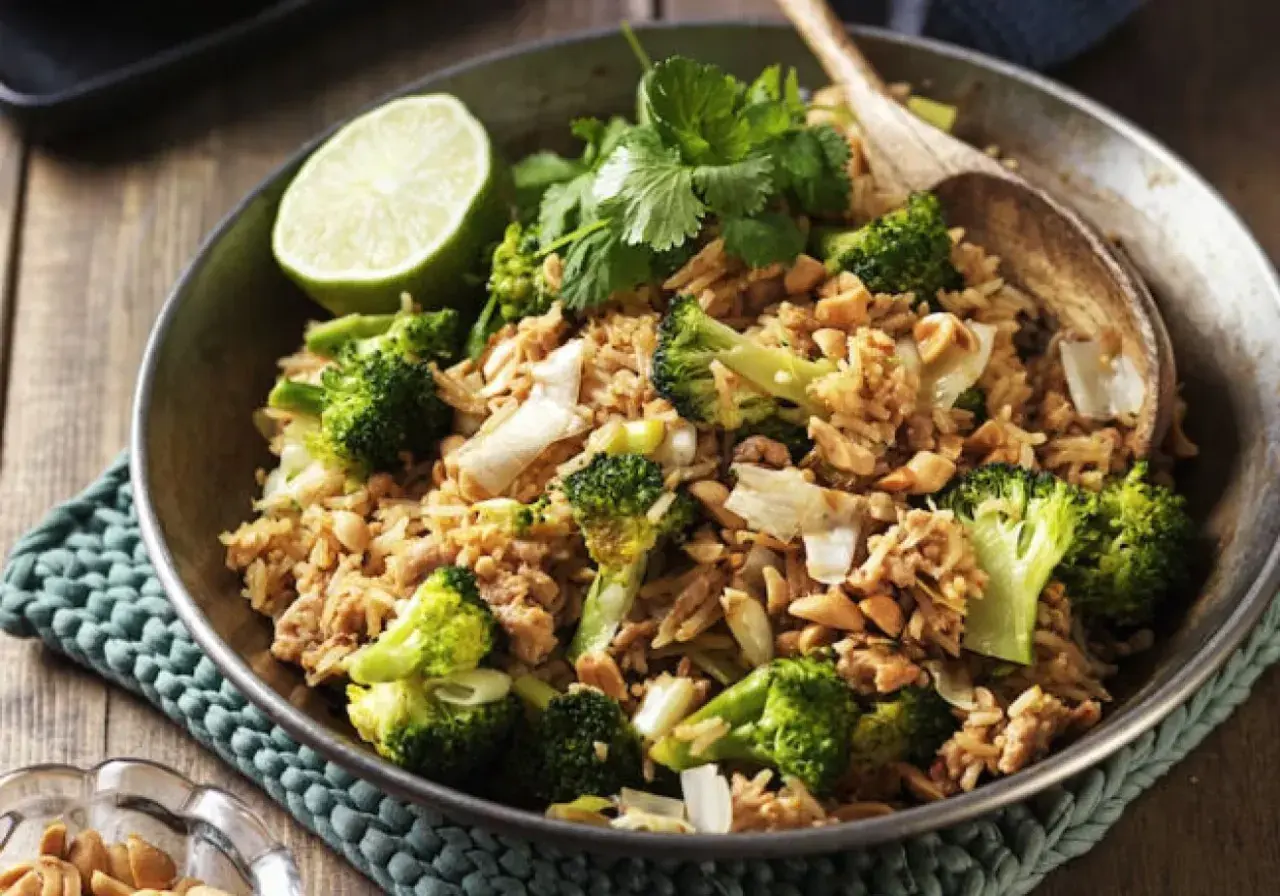 En skål med stekt ris med broccoli, jordnötter och en limeklyfta. En perfekt nyttig lunch.