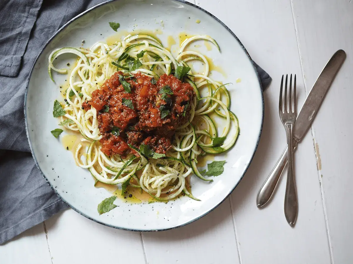 En tallrik med zucchini-spaghetti och köttfärssås, ett av många zucchini nyttiga recept. Garnerad med färska örter och en gnutta citronzest.