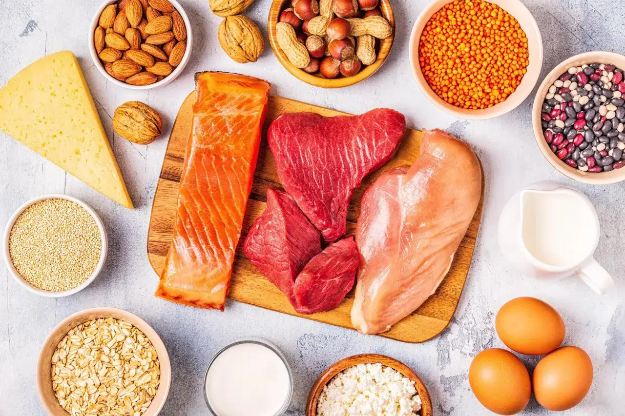 En variation av proteinrika livsmedel: lax, nötkött, kyckling, ägg, ost, nötter, frön, bönor, linser och havregryn. Perfekt för att planera ditt protein per kg.