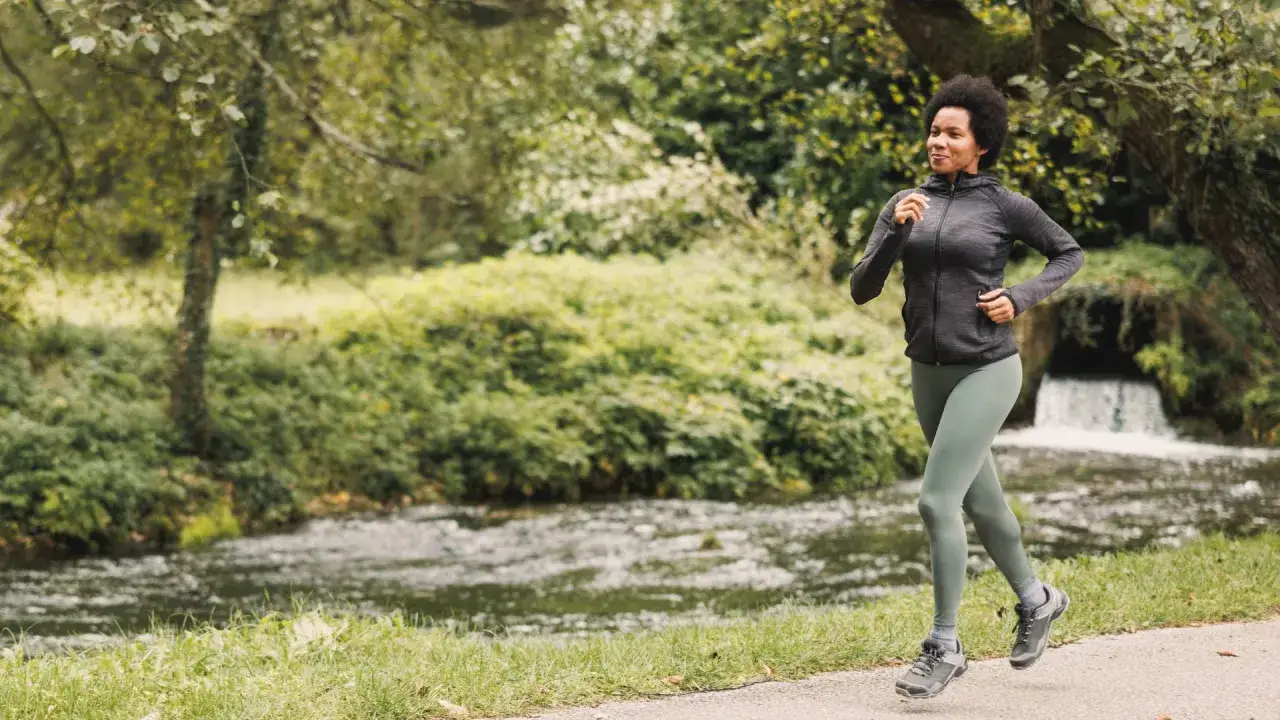 Kvinna joggar längs en bäck med ett litet vattenfall. Frågan är hur snabbt joggar man för att njuta av naturen?