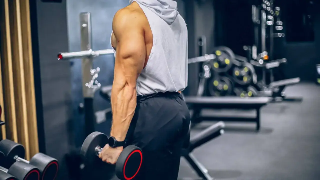 Muskul&ouml;s man utf&ouml;r shrugs med hantlar i ett gym.