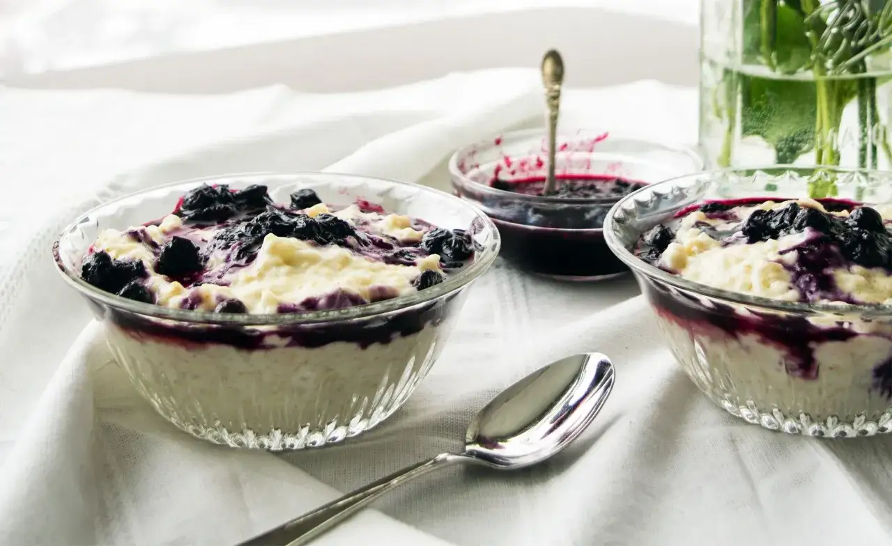 Två skålar med krämig risgrynsgröt toppad med blåbärssylt. En liten skål med mer sylt och en sked står bredvid. En nyttig dessert som passar alla.