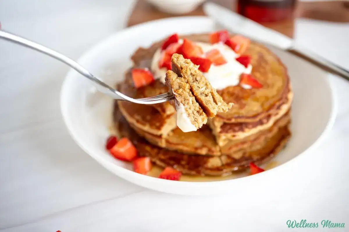 En gaffel lyfter en bit av fluffiga proteinpannkakor, toppade med gr&auml;dde och jordgubbar. Ett perfekt proteinpannkakor recept f&ouml;r en h&auml;lsosam frukost.