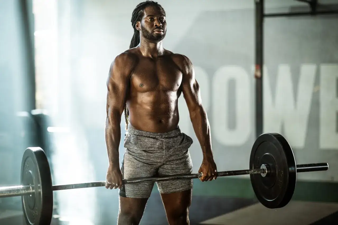 En svettig man med dreadlocks håller i en skivstång i ett gym. Han visar hur mycket muskler man kan bygga på ett år med rätt träning.