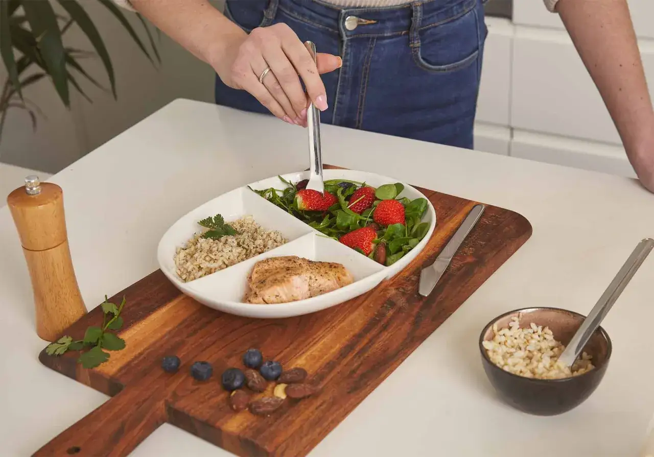En person tar en jordgubbe från en sallad. Måltiden består av lax, ris och en sallad med jordgubbar, vilket kan vara en del av en strategi för att hantera kaloriunderskott symptom.