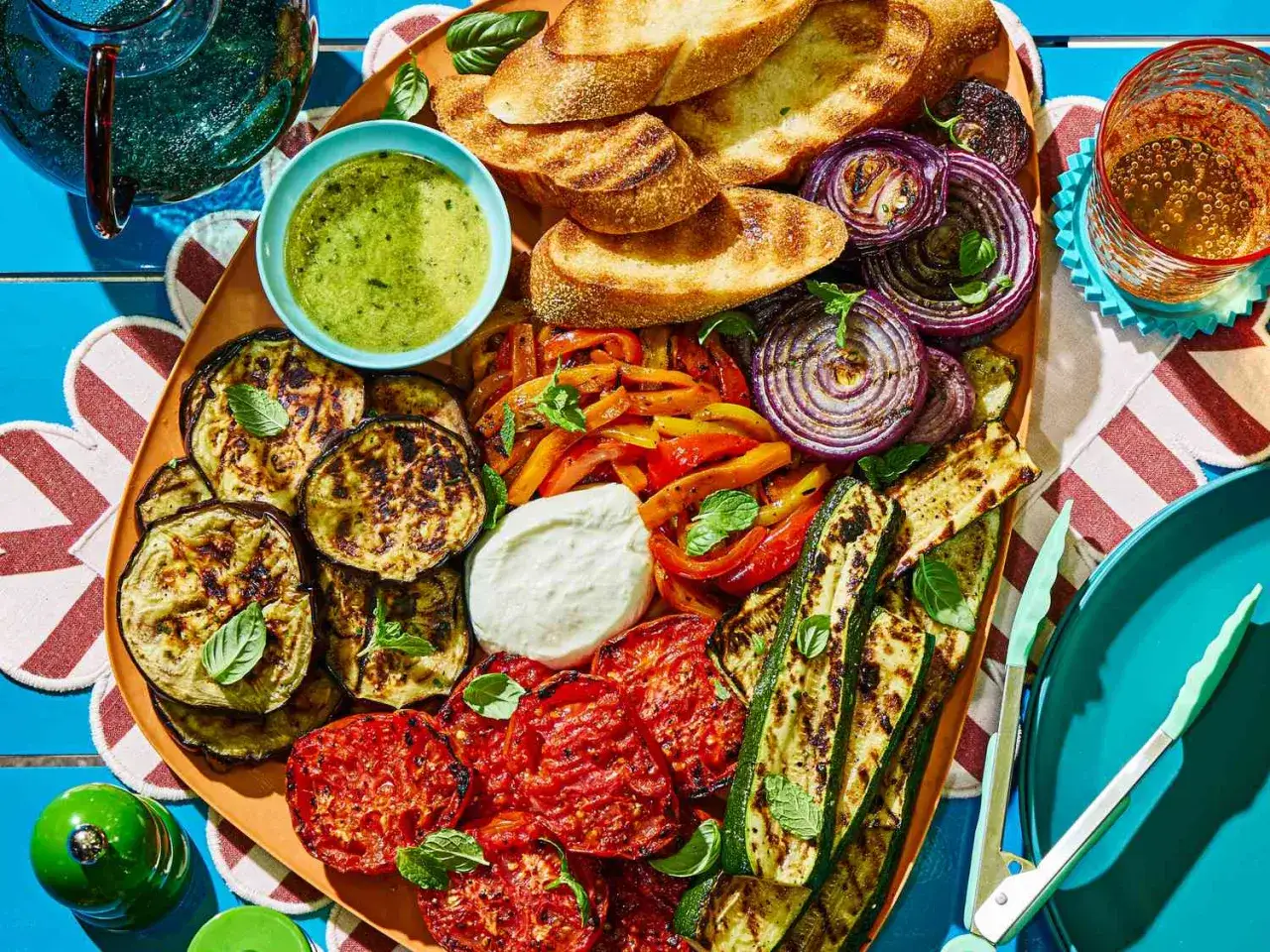 Stor bricka med nyttig grillmat: grillad aubergine, paprika, lök, zucchini, tomater, bröd och en grön sås.