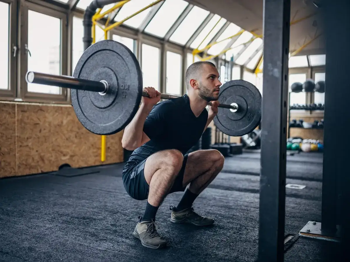 Man utför en djup knäböj med skivstång. En intensiv russian squat routine för att bygga styrka.