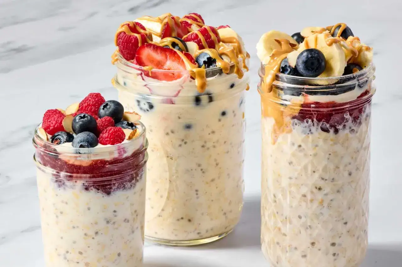 Tre burkar med overnight oats, toppade med bär, nötter och jordnötssmör. En hälsosam frukost som kan hjälpa vid sluta med socker biverkningar.