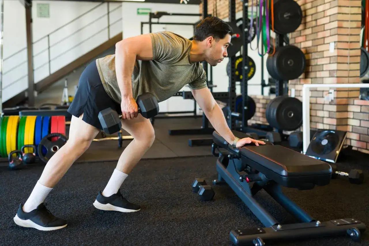 Man utför enarms hantelrodd vid en träningsbänk i ett gym.