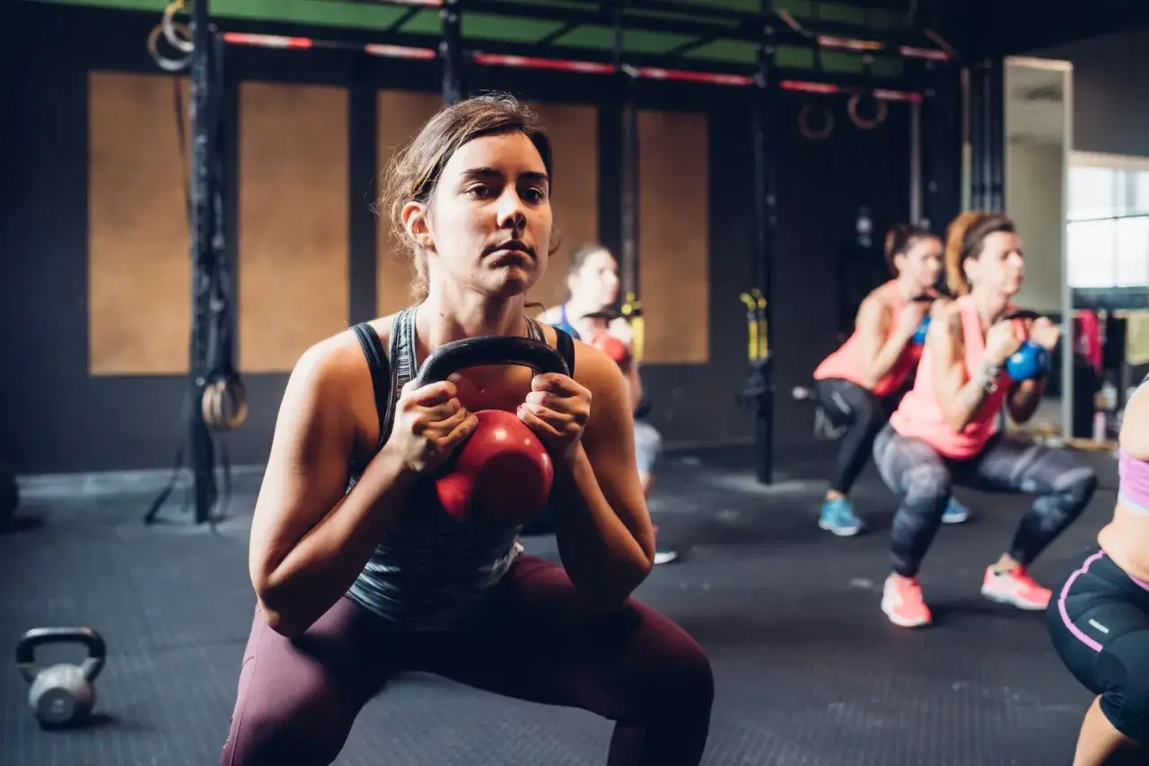 Kvinnor utför kettlebell-knäböj i gymmet. Frågan 