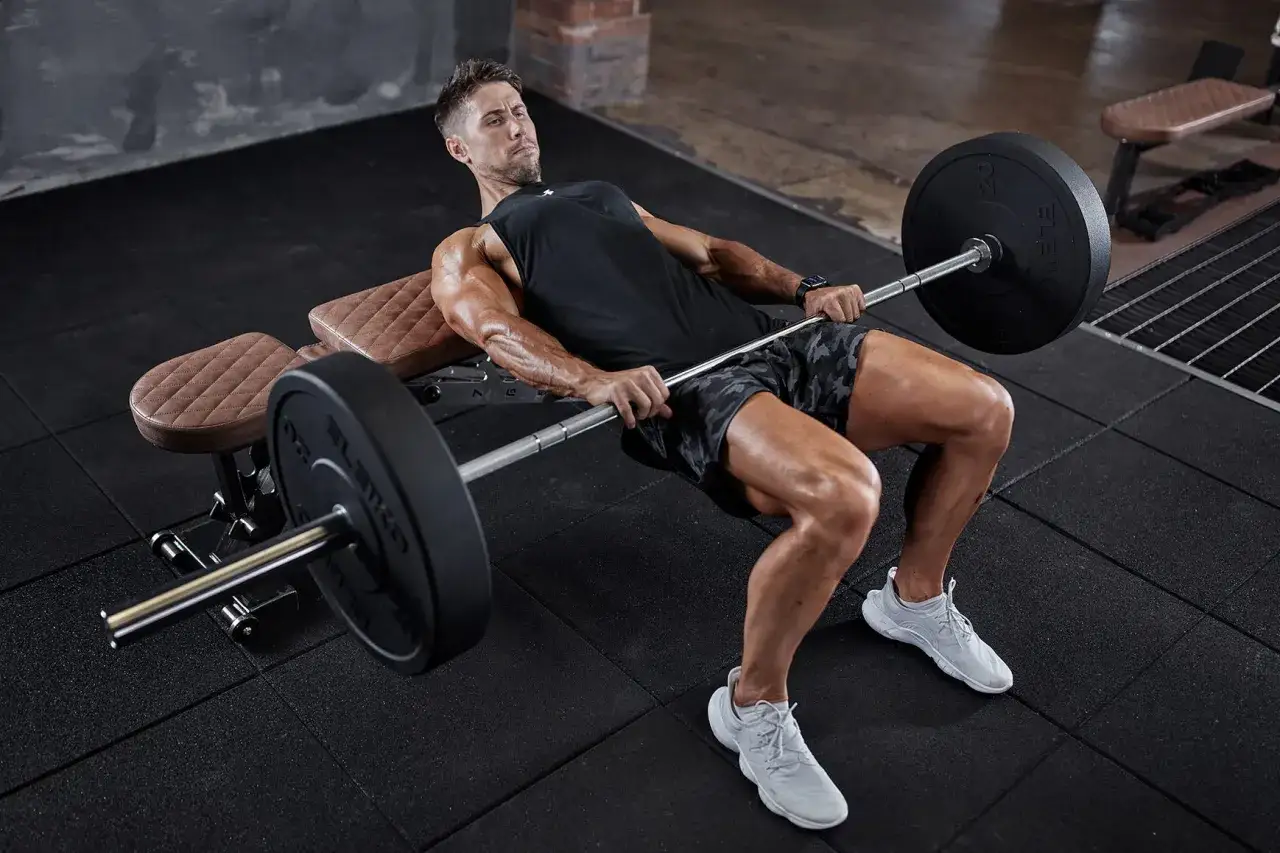 Man utför hip thrust med skivstång på en bänk i ett gym.