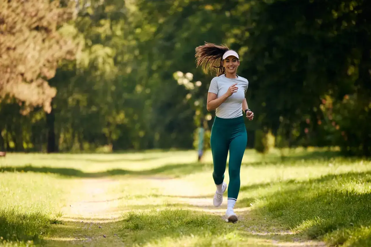 Glad kvinna springer 5 km i parken, njuter av en bra tid i naturen.