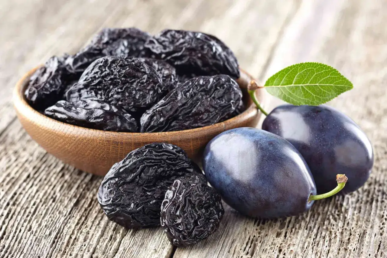 Torkade plommon i en skål och färska plommon på träbord. Plommon nyttigt för magen och fullt av vitaminer.