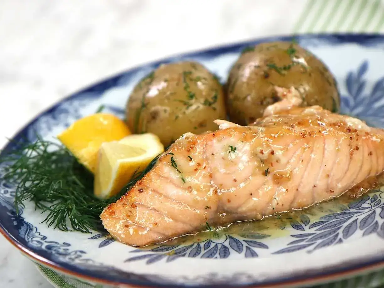 En saftig bit lax, perfekt tillagad från fryst, serveras med dill, citronklyftor och små potatisar på en blåvit tallrik.