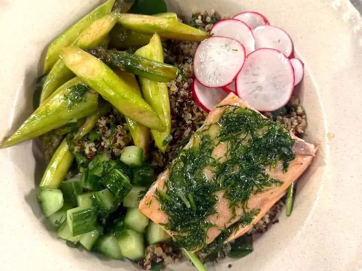 En portion lax med dill serveras på en bädd av quinoa, en bra källa till kolhydrater, tillsammans med sparris, gurka och rädisor.