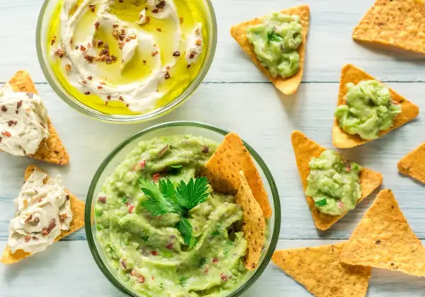 Två skålar med dipp, en med krämig hummus och en med färsk guacamole, serveras med tortillachips. Perfekt för en fiberrik matupplevelse.