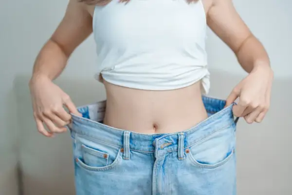 En person visar upp sina för stora jeans, ett tecken på att hon lyckats med hur man går ner i vikt.