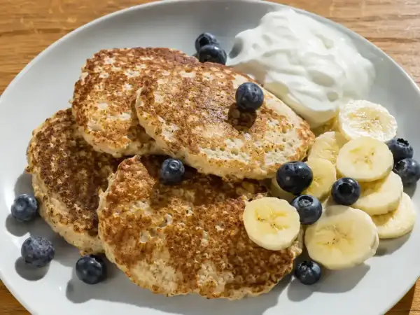 En tallrik med fluffiga bananpannkakor gjorda på havregryn, toppade med färska blåbär, bananskivor och en klick yoghurt. En perfekt frukost!