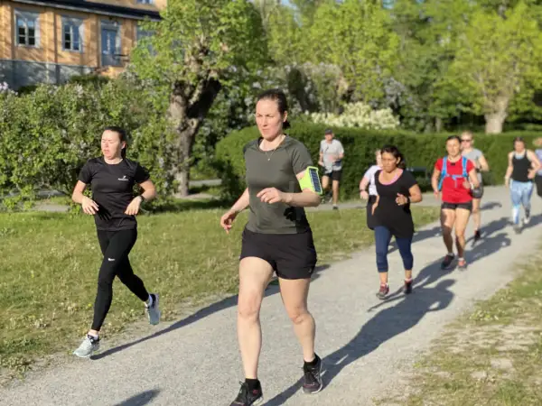En grupp löpare, mestadels kvinnor, tar sig fram på en grusväg i en park. De är på väg att springa en mil i det vackra vårvädret.