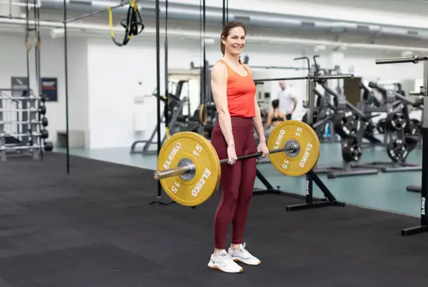 Kvinna i gym utför marklyft med skivstång. Träning för marklyft muskler.