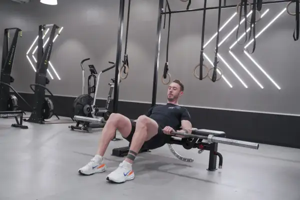 Man utför hip thrust med skivstång på en bänk i ett modernt gym.